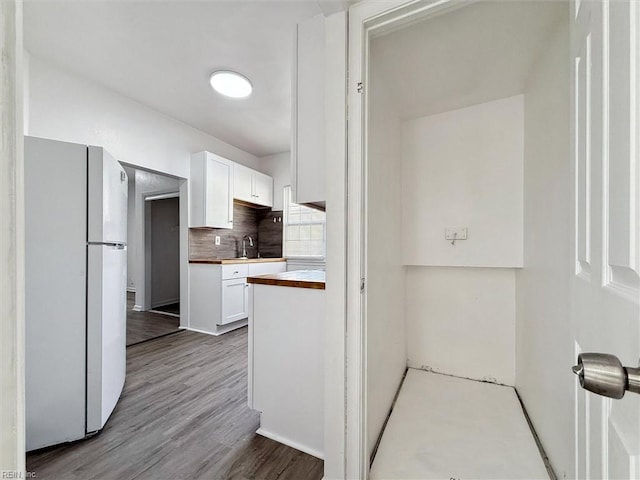 kitchen featuring a sink, freestanding refrigerator, white cabinetry, wood finished floors, and tasteful backsplash