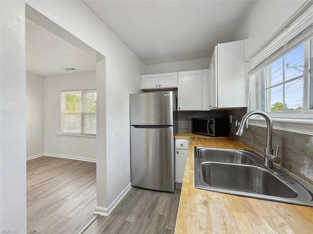 kitchen with appliances with stainless steel finishes, a sink, white cabinetry, baseboards, and light wood-type flooring