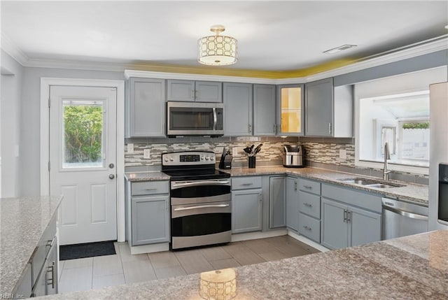 kitchen featuring light stone countertops, a sink, gray cabinets, stainless steel appliances, and decorative backsplash