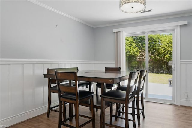 dining area with crown molding, wainscoting, a decorative wall, wood finished floors, and visible vents