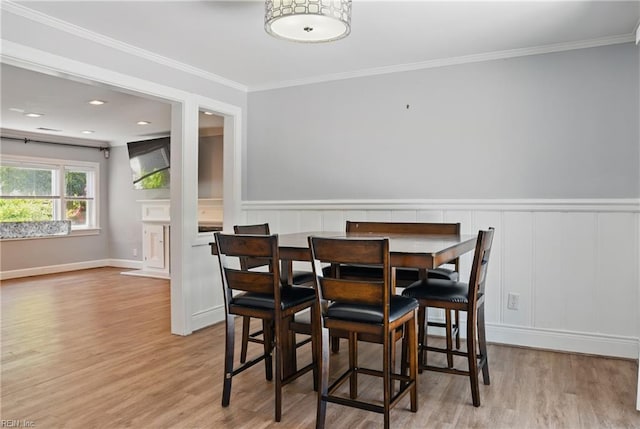 dining area featuring ornamental molding, a decorative wall, and wood finished floors