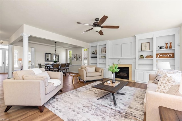 living area featuring light wood-style floors, a fireplace with flush hearth, decorative columns, and a ceiling fan