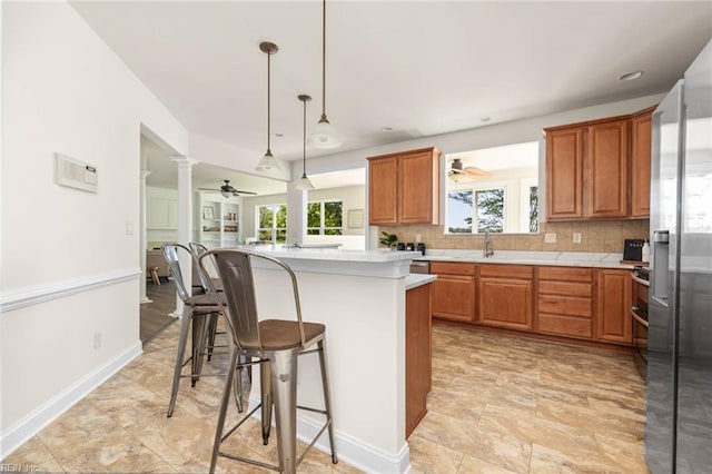 kitchen with plenty of natural light, a breakfast bar area, a ceiling fan, light countertops, and ornate columns