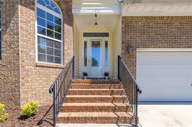 view of exterior entry with a garage, concrete driveway, and brick siding