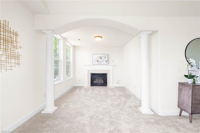 unfurnished living room featuring decorative columns, a glass covered fireplace, baseboards, arched walkways, and carpet flooring