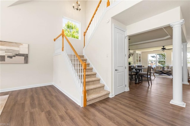 stairway with a ceiling fan, a towering ceiling, wood finished floors, baseboards, and ornate columns