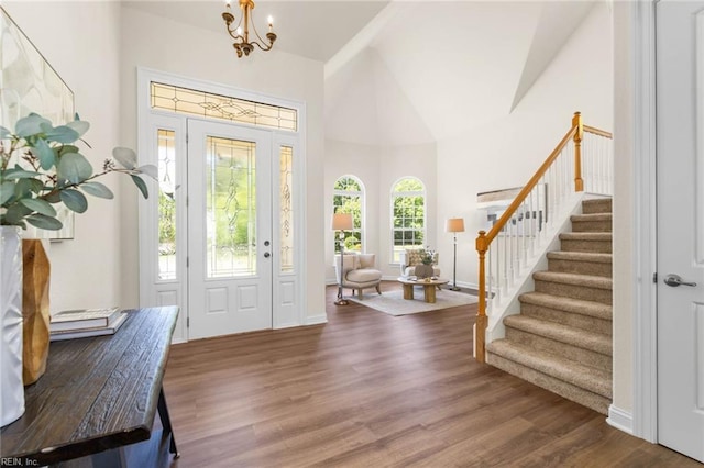 entryway featuring stairs, wood finished floors, baseboards, high vaulted ceiling, and a chandelier