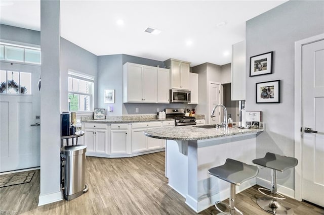 kitchen with a kitchen breakfast bar, a sink, white cabinets, a peninsula, and stainless steel appliances