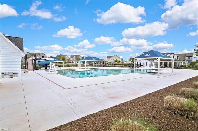community pool featuring a gazebo, a water slide, a residential view, and a patio area
