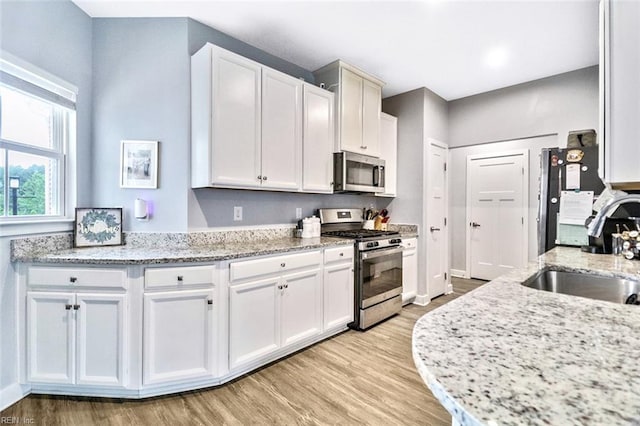 kitchen with light wood-style floors, a sink, white cabinets, and stainless steel appliances