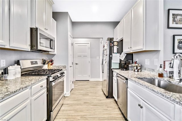 kitchen with light stone countertops, a sink, light wood-style flooring, stainless steel appliances, and baseboards