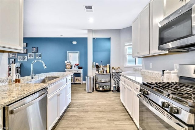 kitchen featuring visible vents, light wood-type flooring, a sink, light stone counters, and stainless steel appliances