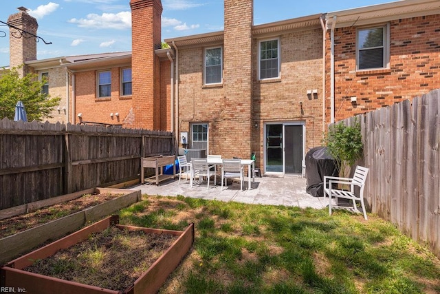rear view of house featuring a garden, a patio, a fenced backyard, brick siding, and a yard