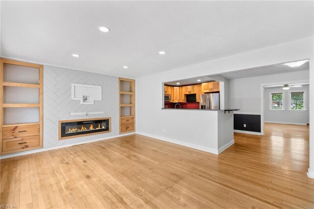 unfurnished living room with a sink, light wood-style floors, a glass covered fireplace, recessed lighting, and baseboards