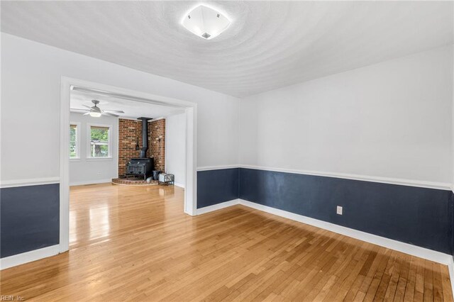 unfurnished room featuring baseboards, a ceiling fan, a wood stove, and light wood-style flooring