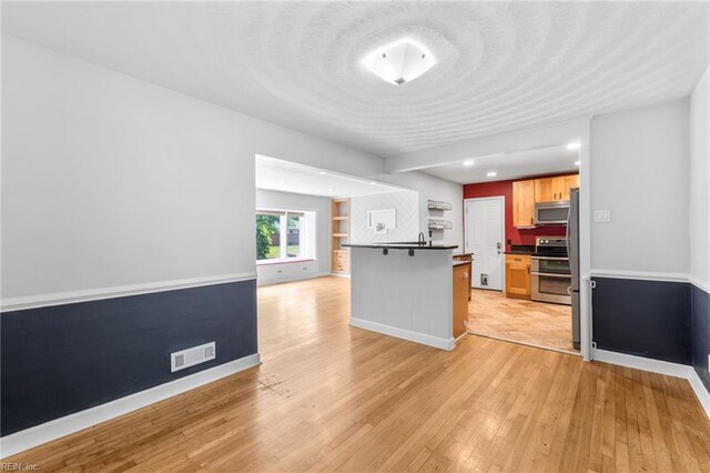 kitchen featuring visible vents, dark countertops, baseboards, light wood finished floors, and stainless steel appliances