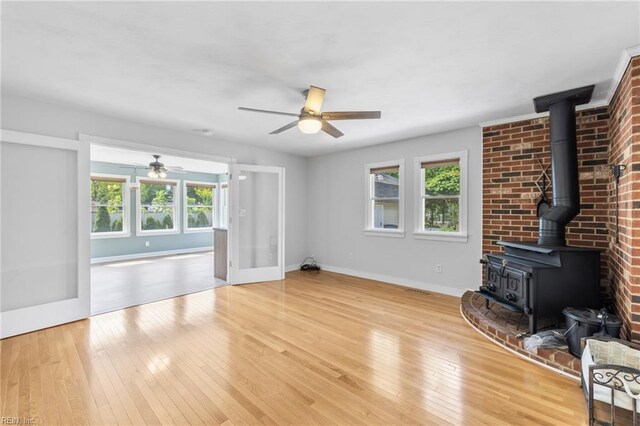 unfurnished living room with ceiling fan, hardwood / wood-style flooring, baseboards, and a wood stove