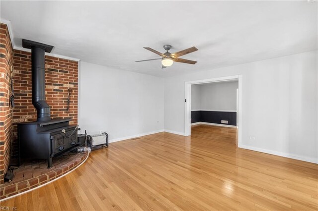 unfurnished living room featuring baseboards, a wood stove, a ceiling fan, and wood finished floors