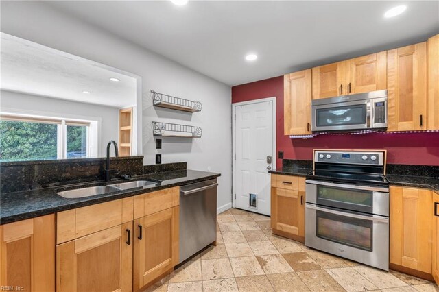 kitchen with baseboards, recessed lighting, a sink, dark stone countertops, and appliances with stainless steel finishes