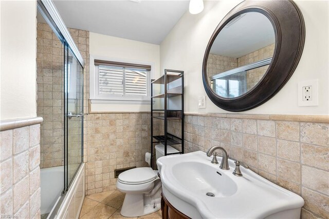 full bath with wainscoting, toilet, tile patterned floors, tiled shower / bath, and tile walls