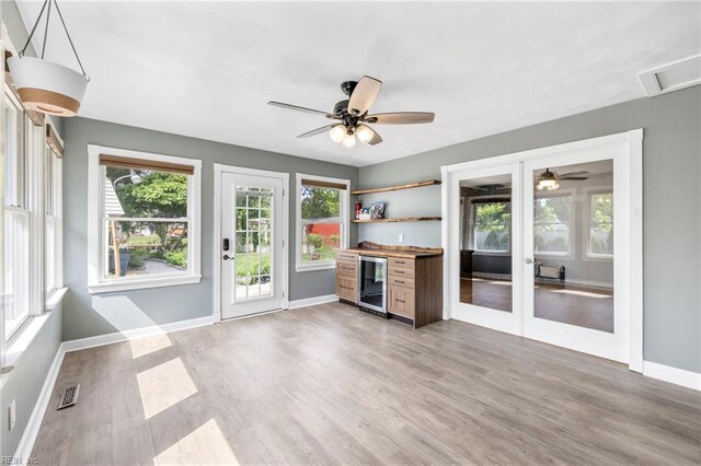unfurnished living room featuring a dry bar, baseboards, light wood-type flooring, wine cooler, and visible vents
