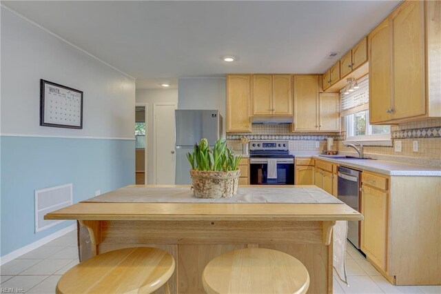 kitchen with light brown cabinetry, light countertops, under cabinet range hood, light tile patterned floors, and stainless steel appliances