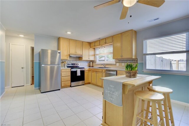 kitchen featuring a sink, appliances with stainless steel finishes, light brown cabinets, and under cabinet range hood