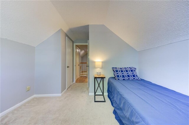 carpeted bedroom with a textured ceiling, vaulted ceiling, and baseboards