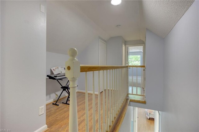 hallway featuring baseboards, vaulted ceiling, wood finished floors, and an upstairs landing