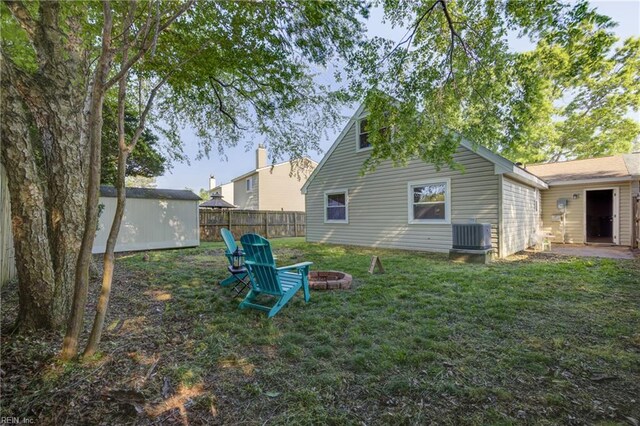 back of house featuring an outdoor structure, fence, central AC unit, a lawn, and an outdoor fire pit