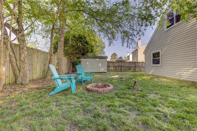 view of yard featuring a fenced backyard, a fire pit, a shed, and an outbuilding