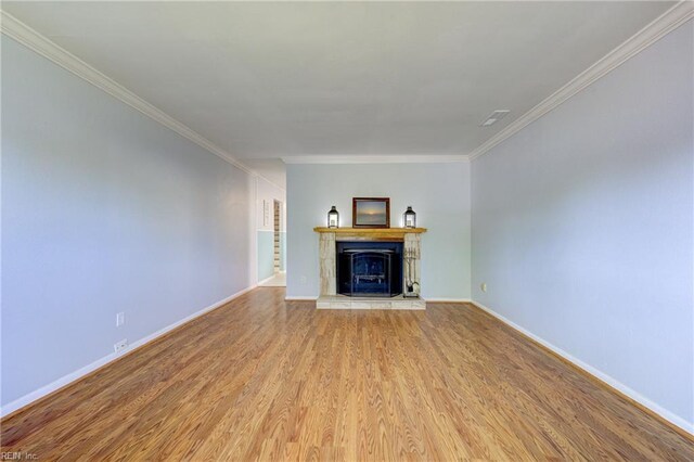 unfurnished living room with crown molding, baseboards, light wood-style floors, and a fireplace with raised hearth