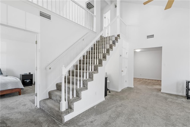 staircase featuring visible vents, baseboards, a high ceiling, a ceiling fan, and carpet