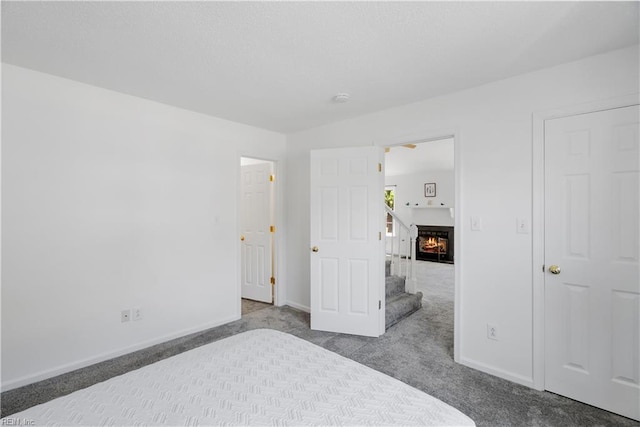 unfurnished bedroom featuring baseboards, carpet, and a warm lit fireplace