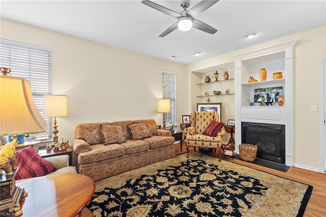 living area featuring a fireplace with flush hearth, ceiling fan, wood finished floors, and a wealth of natural light