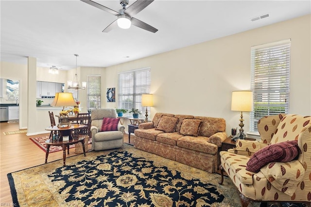 living room with a wealth of natural light, ceiling fan with notable chandelier, wood finished floors, and visible vents