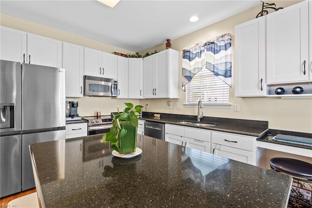 kitchen with a sink, dark stone counters, stainless steel appliances, recessed lighting, and white cabinetry