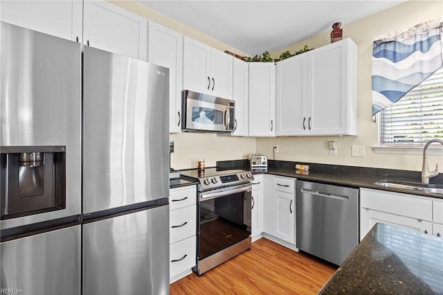kitchen with a sink, appliances with stainless steel finishes, light wood finished floors, and white cabinetry