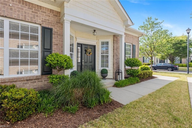 view of exterior entry featuring a lawn, a porch, and brick siding