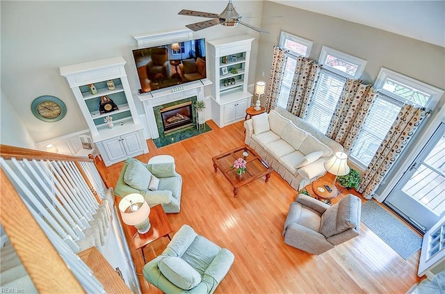 living room featuring a towering ceiling, ceiling fan, wood finished floors, and a fireplace