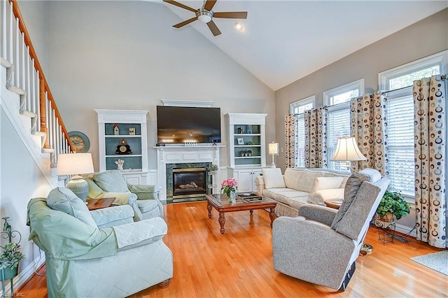living room with ceiling fan, a fireplace, wood finished floors, stairway, and high vaulted ceiling