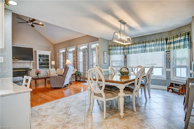 dining room featuring a glass covered fireplace, light tile patterned flooring, baseboards, ceiling fan, and high vaulted ceiling