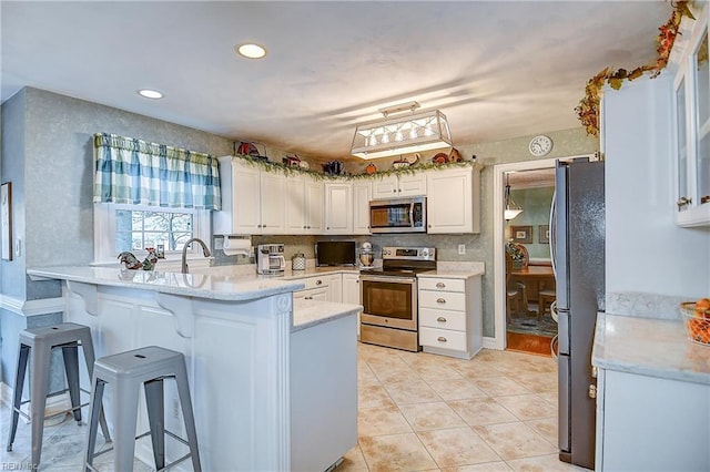 kitchen with a kitchen breakfast bar, light tile patterned floors, white cabinets, a peninsula, and stainless steel appliances