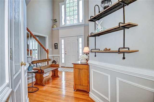 foyer featuring wainscoting, light wood-type flooring, a high ceiling, a decorative wall, and stairs