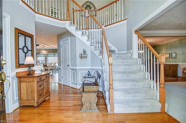 staircase with wood finished floors, a decorative wall, a high ceiling, and a wainscoted wall