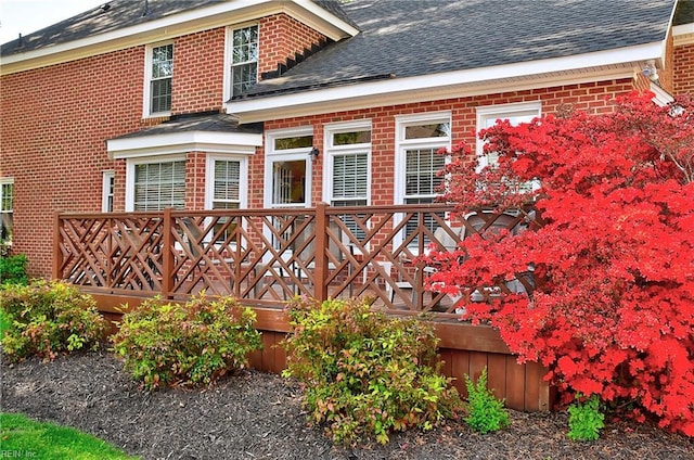 view of side of home with brick siding, roof with shingles, and a deck