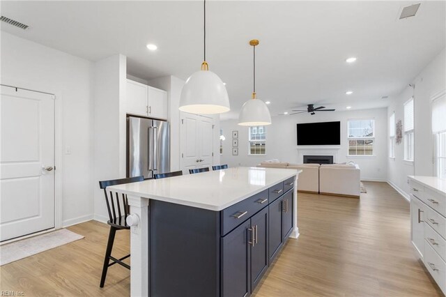 kitchen featuring visible vents, a fireplace, ceiling fan, high end refrigerator, and light wood-style flooring