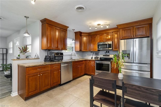 kitchen with stainless steel appliances, brown cabinets, light stone counters, a sink, and pendant lighting