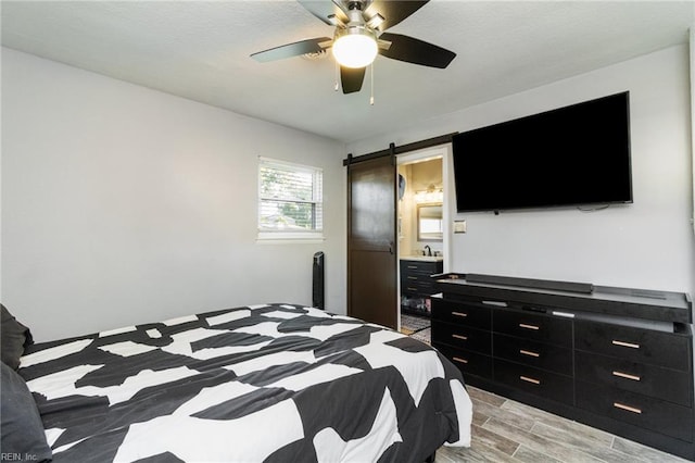 bedroom featuring a barn door, light wood-style floors, a ceiling fan, and ensuite bath
