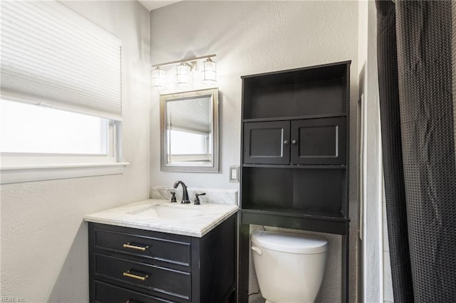 bathroom with toilet, vanity, and a textured wall
